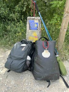 A Camino de Santiago road sign with backpacks and a walking stick resting beside it.