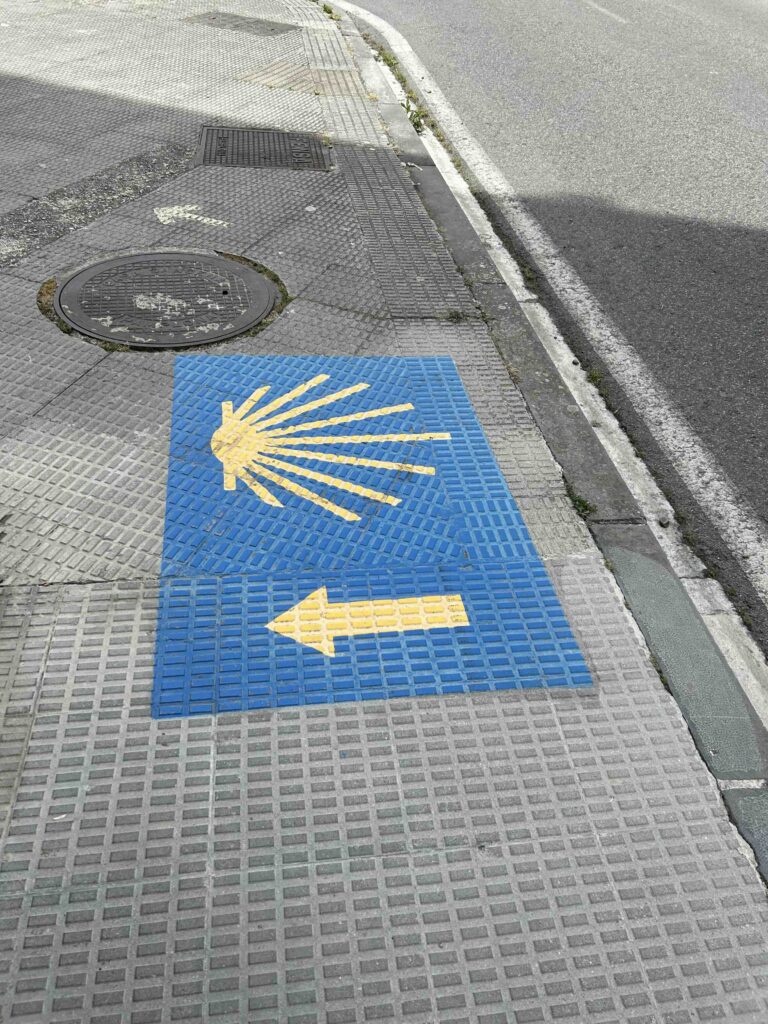 A Camino sign on the floor featuring the yellow shell and arrow, guiding pilgrims on The French Way