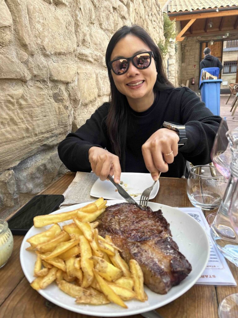 A woman enjoying a big plate of steak and fries after a long day on the Camino de Santiago.