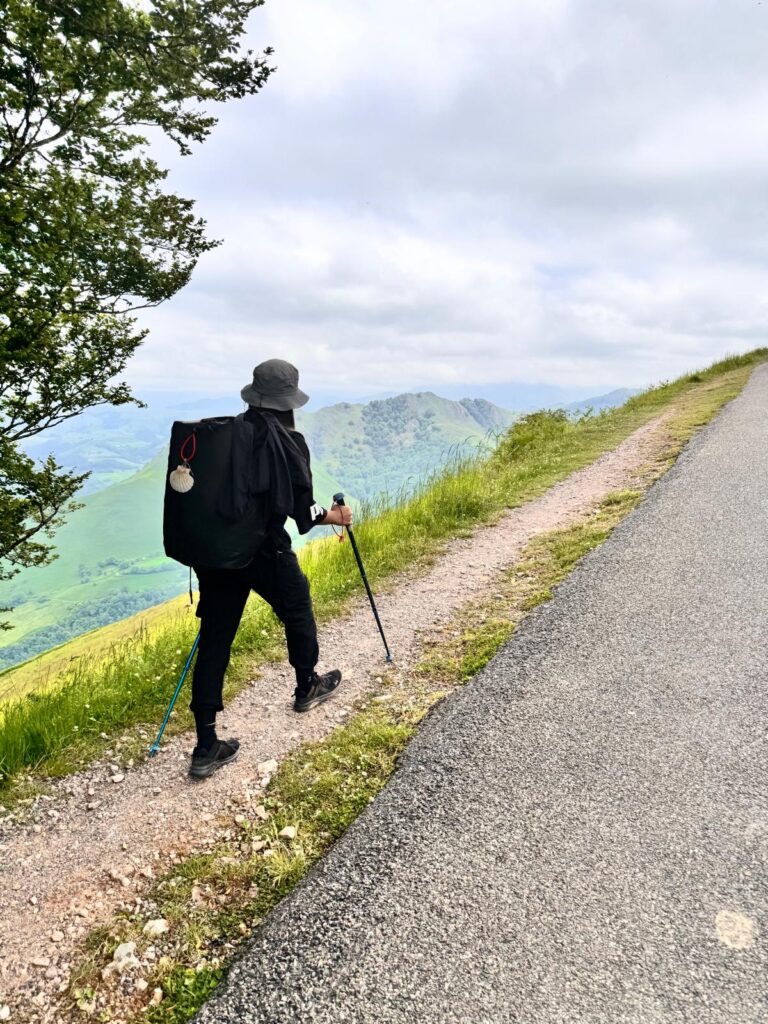 Pilgrims walking uphill on the Camino Frances just outside Saint-Jean-Pied-de-Port, surrounded by green hills.