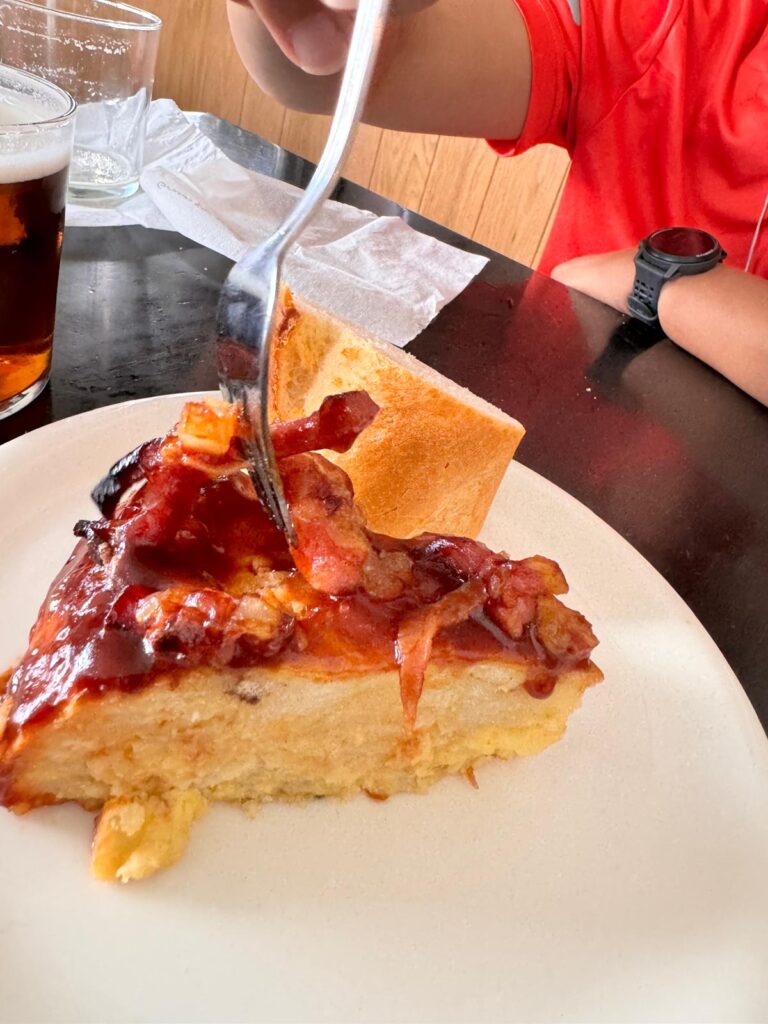 Slice of layered potato pie with crispy bacon on top, enjoyed on the Camino de Santiago